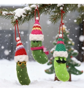 Close-up of knit Christmas pickle ornaments with colorful hats hanging on snowy pine branches