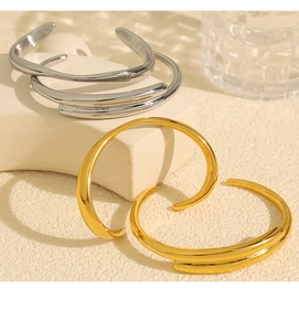 Polished gold and silver C-shaped open cuffs displayed on a minimalist geometric stand