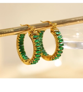Nahaufnahme von Vintage Gold-Creolen mit grünen Smaragdschliff-Steinen auf einem Ständer