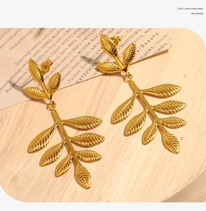 Detail shot of golden leaf dangle earrings with delicate textures on light wood