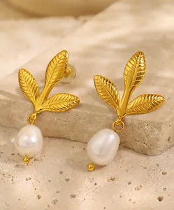 Detailed close-up of golden leaf earrings with white baroque pearl drops on stone background