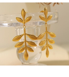Detailed view of golden leaf earrings with delicate vein textures on a glass stand