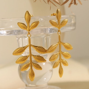 Elegant gold leaf dangle earrings with nature-inspired design on glass stand