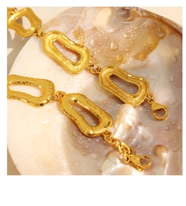 Dettaglio macro di un bracciale a catena dorata con trama martellata su sfondo di conchiglia