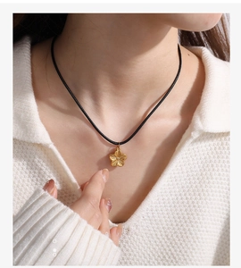 Detailed view of an 18K gold floral pendant on a black cord worn with a white sweater