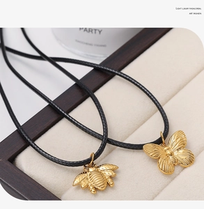 Detailed view of 18K gold plated bee and butterfly pendants on black woven cord