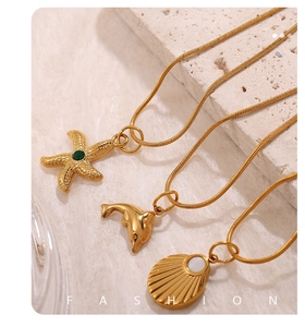 Detalle macro de colgantes dorados de estrella de mar, delfín y concha con gemas verdes