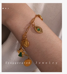 Detail of 18K gold-plated paperclip bracelet with evil eye and coin charms on wrist