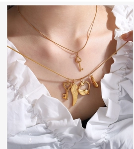 Close-up of a layered gold necklace set with heart-key and angel wings charms on a model