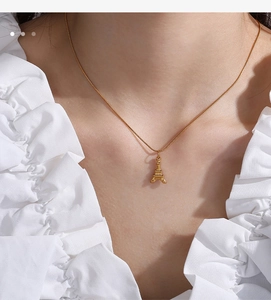 Close-up of a gold Eiffel Tower pendant necklace worn by a model in a white top