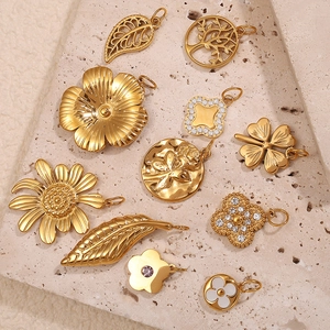 Assorted gold stainless steel charms with floral designs on a stone display board