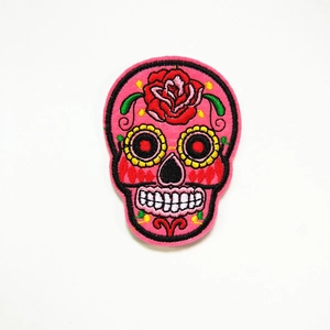 Detail van borduurwerk van een roze suikerschedel met rode rozen en bloemrijke ogen