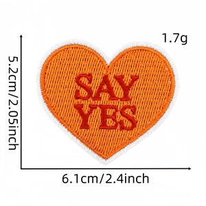 Détail de l'écusson brodé en forme de cœur orange avec texte SAY YES rouge et bord blanc