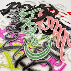 Detailed close-up of colorful cursive alphabet embroidery patches with fine stitching