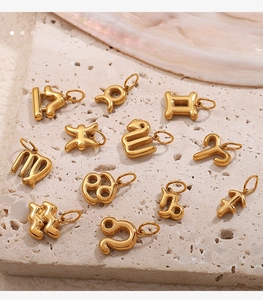 Dettaglio dei ciondoli zodiacali placcati in oro 18K disposti su una superficie in pietra