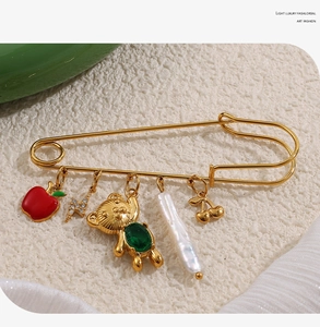 Détail d'une broche épingle dorée avec des breloques variées comme pomme et perle