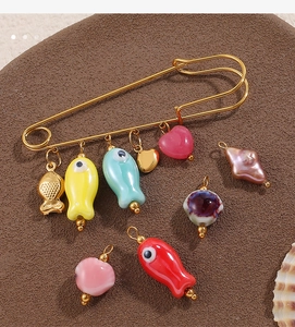 Détail d'une épingle de sûreté en acier avec pendentifs poissons et perles sur support