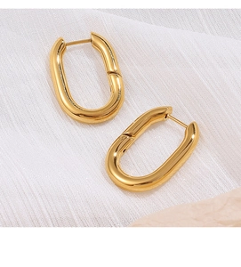 Boucles d'oreilles ovales dorées en acier poli sur un tissu texturé blanc élégant