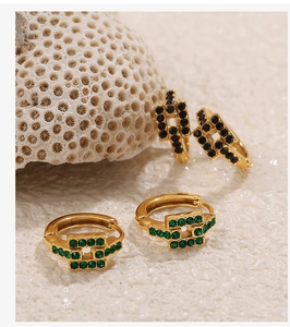 Dettaglio di orecchini placcati oro 18K con zirconi neri e verdi su corallo bianco