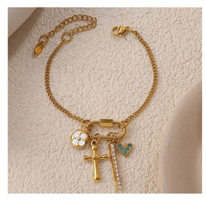 Détail du bracelet doré avec pendentifs fleur, croix, barre zircon et cœur bleu