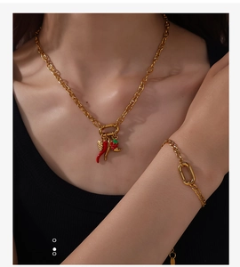 Close-up of gold chain jewelry set featuring red chili and strawberry enamel charms