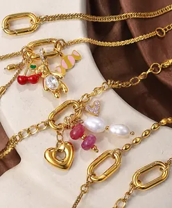 Close-up of gold charm bracelets with red cherry, pearl, and heart pendants on silk