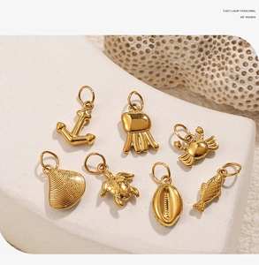 Close-up of golden nautical charms including anchor and sea turtle on a white stone background