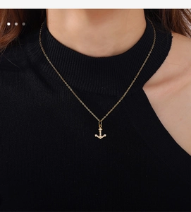 Close-up of golden anchor pendant necklace with white rhinestones on a black top