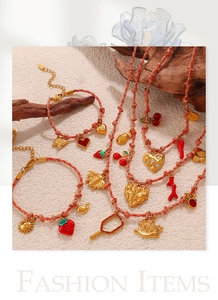 Detalle de pulseras y collares rojos con colgantes dorados de frutas y animales