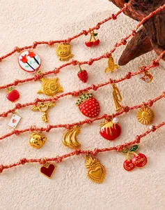 Detalle de pulsera de acero inoxidable con dijes de oro de 18K como fresa y cereza