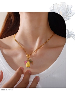 Detail of gold necklace with enamel flower, suitcase and palm tree pendants on neck