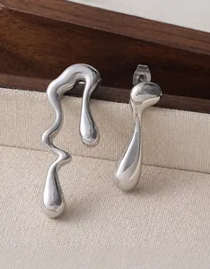 Macro detail of asymmetric liquid silver earrings on a rustic wood and fabric tray