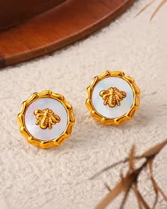 Macro shot of 18K gold earrings featuring a 3D bee relief on white mother-of-pearl