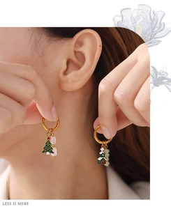 Detail of Christmas tree and house enamel earrings worn by a model in warm light