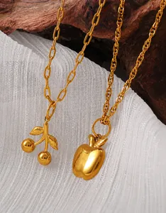Gros plan de pendentifs cerise et pomme dorés sur colliers devant un fond en bois