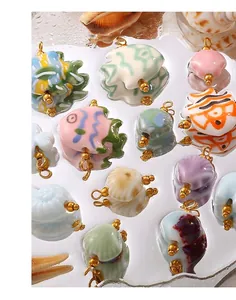 Detail of colorful ceramic fish and shell charms with 18K gold plated loops on white surface