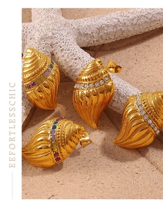 Close-up of golden shell earrings with multi-colored crystals on sand background