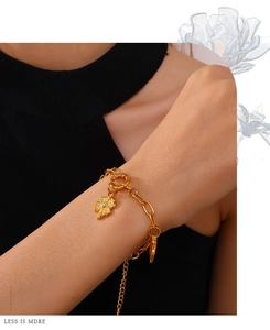 Close-up of a gold chain bracelet with a sparkling four-leaf clover charm on a model's wrist