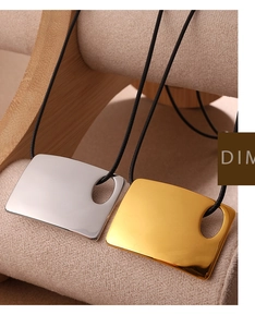 Detalle macro de colgantes cuadrados geométricos en oro y plata con cordón negro