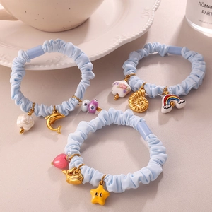 Three light blue scrunchies with marine charms like sea turtles and shells on a desk