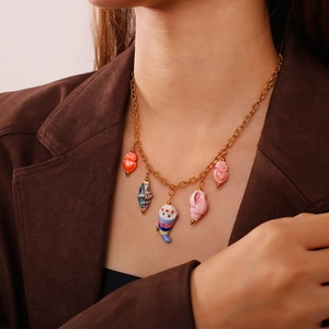 Golden chain necklace featuring colorful ceramic heart and shell charms worn on a model