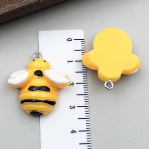 Vue détaillée de petits pendentifs abeilles en résine avec échelle de mesure de 2,5 cm