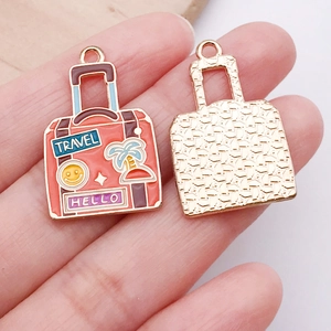 Close-up of enamel suitcase charms with Travel and Hello text for DIY jewelry making