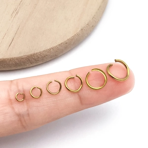 Detailed comparison of six sizes of gold stainless steel open jump rings on a finger