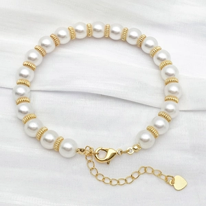 Detail of white pearl bracelet with gold textured beads and a heart charm on white silk