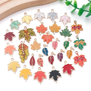 Flat lay of colorful enamel maple leaf pendants in diverse autumn colors with gold plating