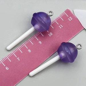 Détail macro de breloques sucettes en résine violette pailletée avec mesures sur une règle