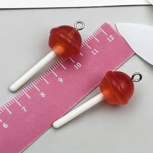 Vue détaillée de deux pendentifs sucettes en résine rouge avec paillettes et anneaux