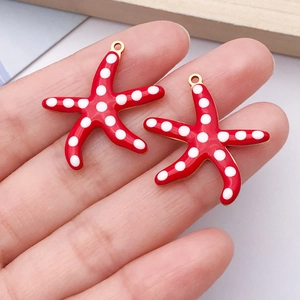 Detailed macro view of red enamel starfish charms with white dots and gold metal loops
