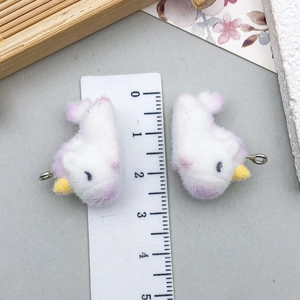 Detailed macro view showing a pair of white flocked unicorn charms with a size ruler